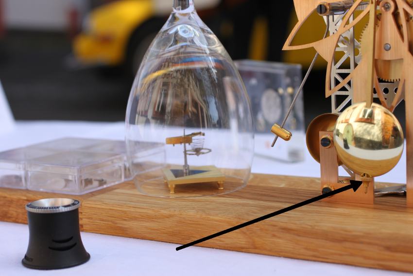Arrow pointing to the regulating nut below the pendulum bob